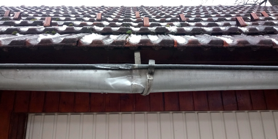 Damaged rain gutter beneath a tiled roof (78370)